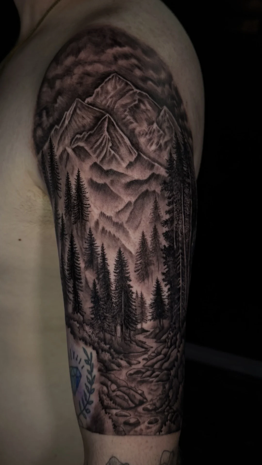 A black-and-gray mountain landscape framed by dense pine trees and curved decorative details on the arm.