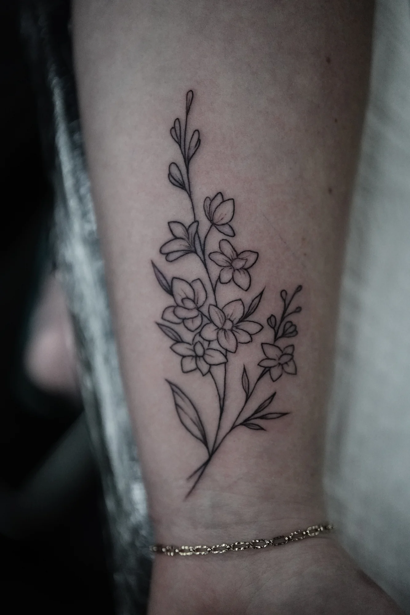 A delicate linework stem with small flowers, buds and leaves near the wrist.