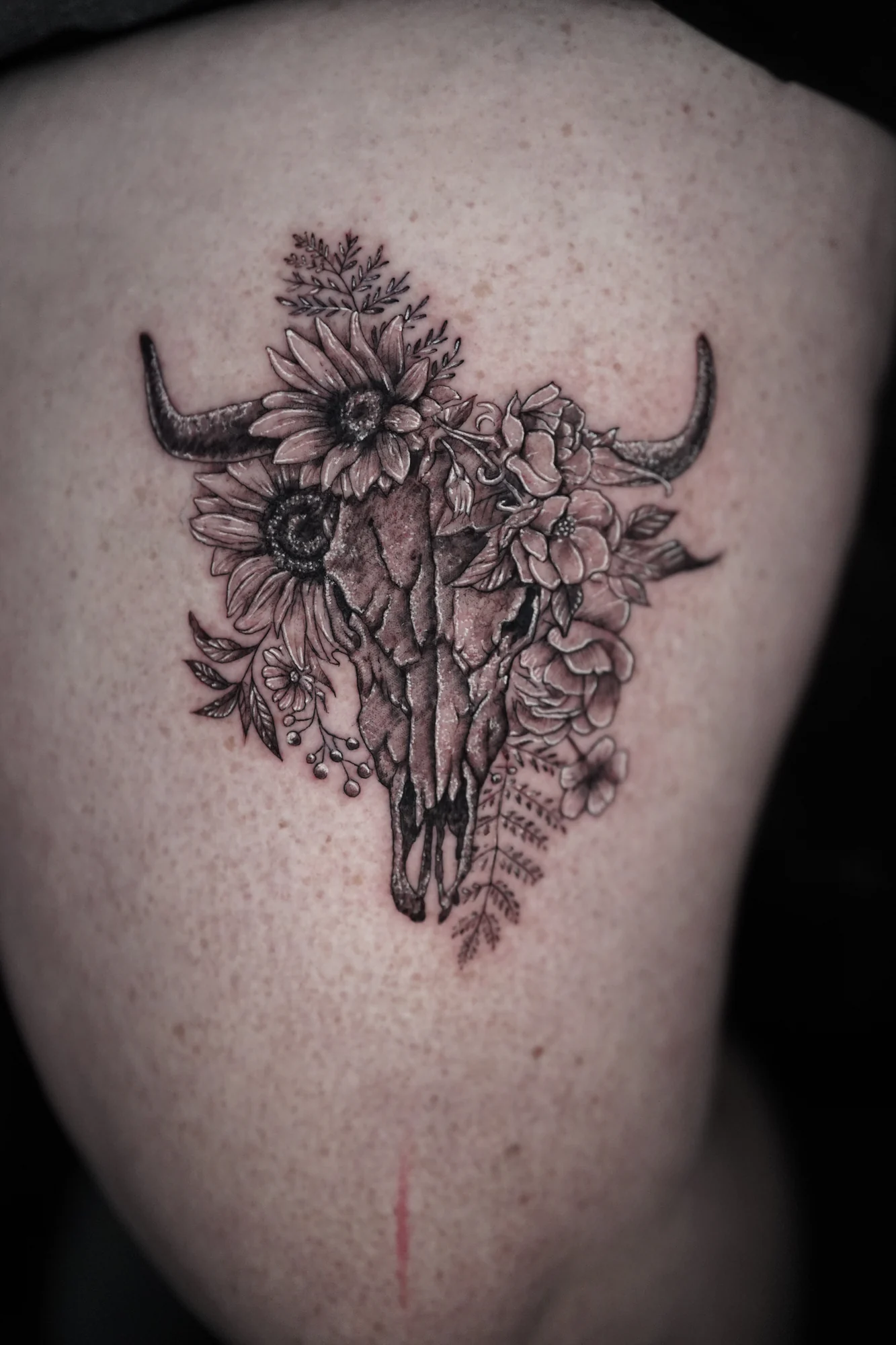 A horned cattle skull surrounded by detailed flowers, leaves and small buds in black linework.