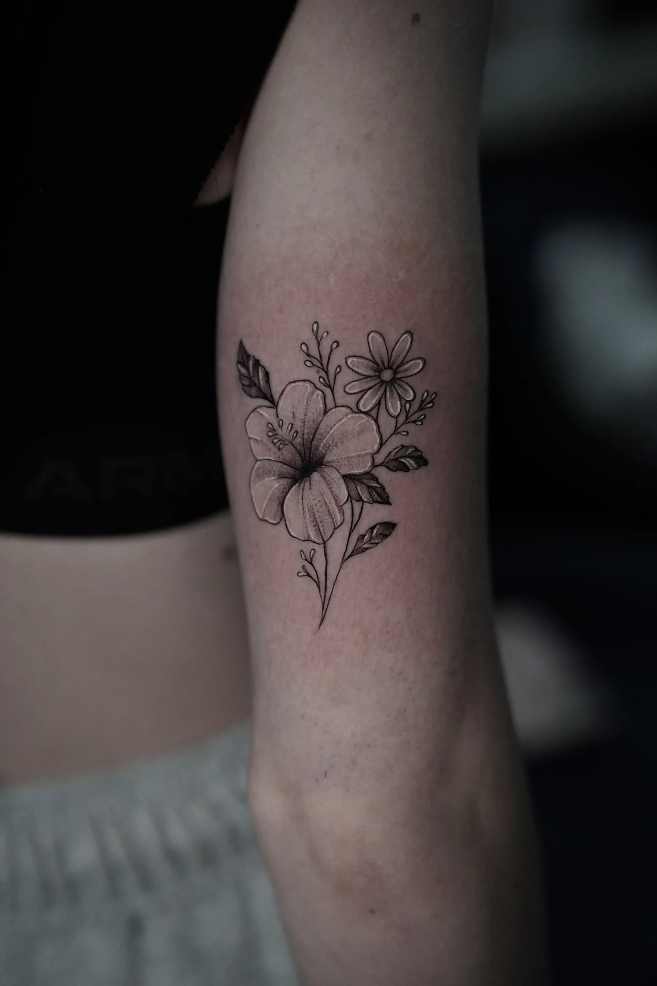 A small bouquet of sunflower-like blooms and leaves drawn in fine black lines on the forearm.
