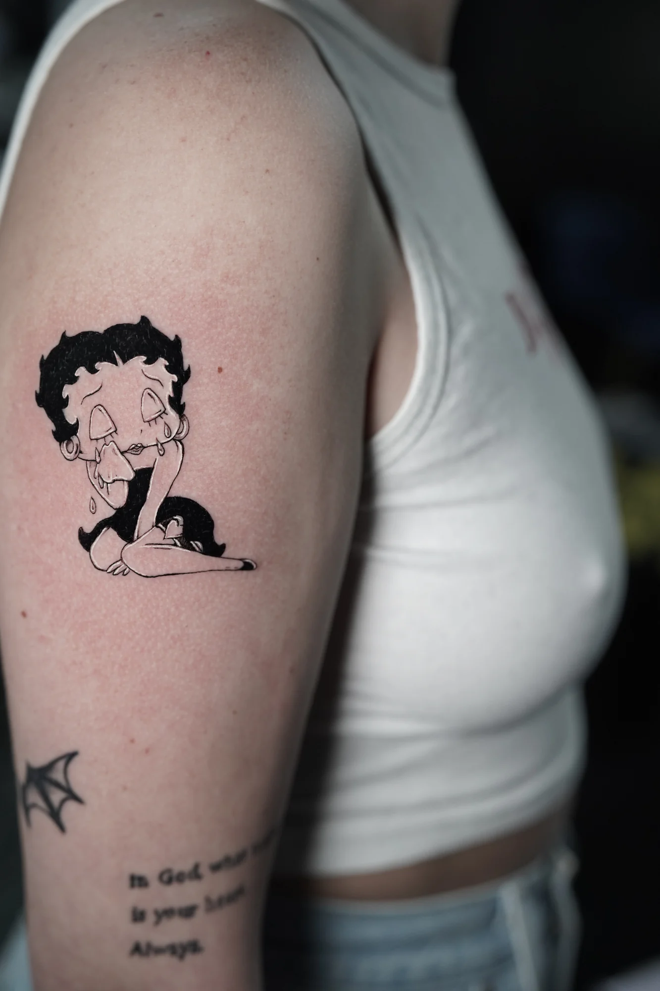 A small Betty Boop character tattoo in black linework and shading on the upper arm.
