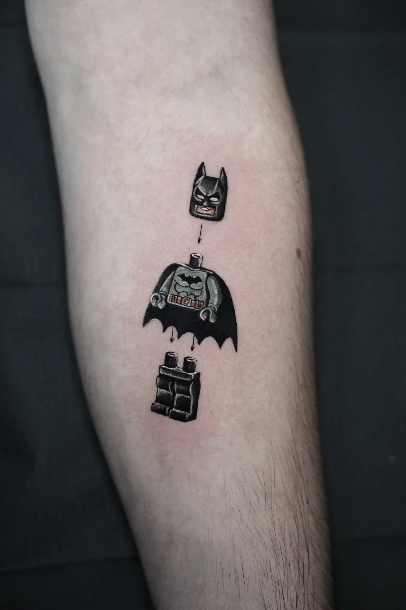 A small LEGO-style Batman tattoo with the mask, torso and legs separated vertically.
