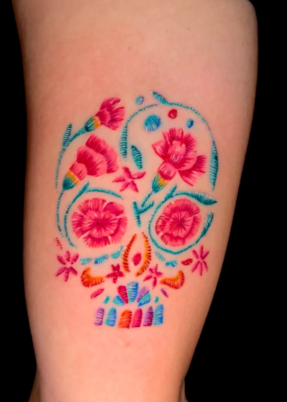 A colorful decorative skull formed from pink and red flowers, blue dots and turquoise ornamental lines.