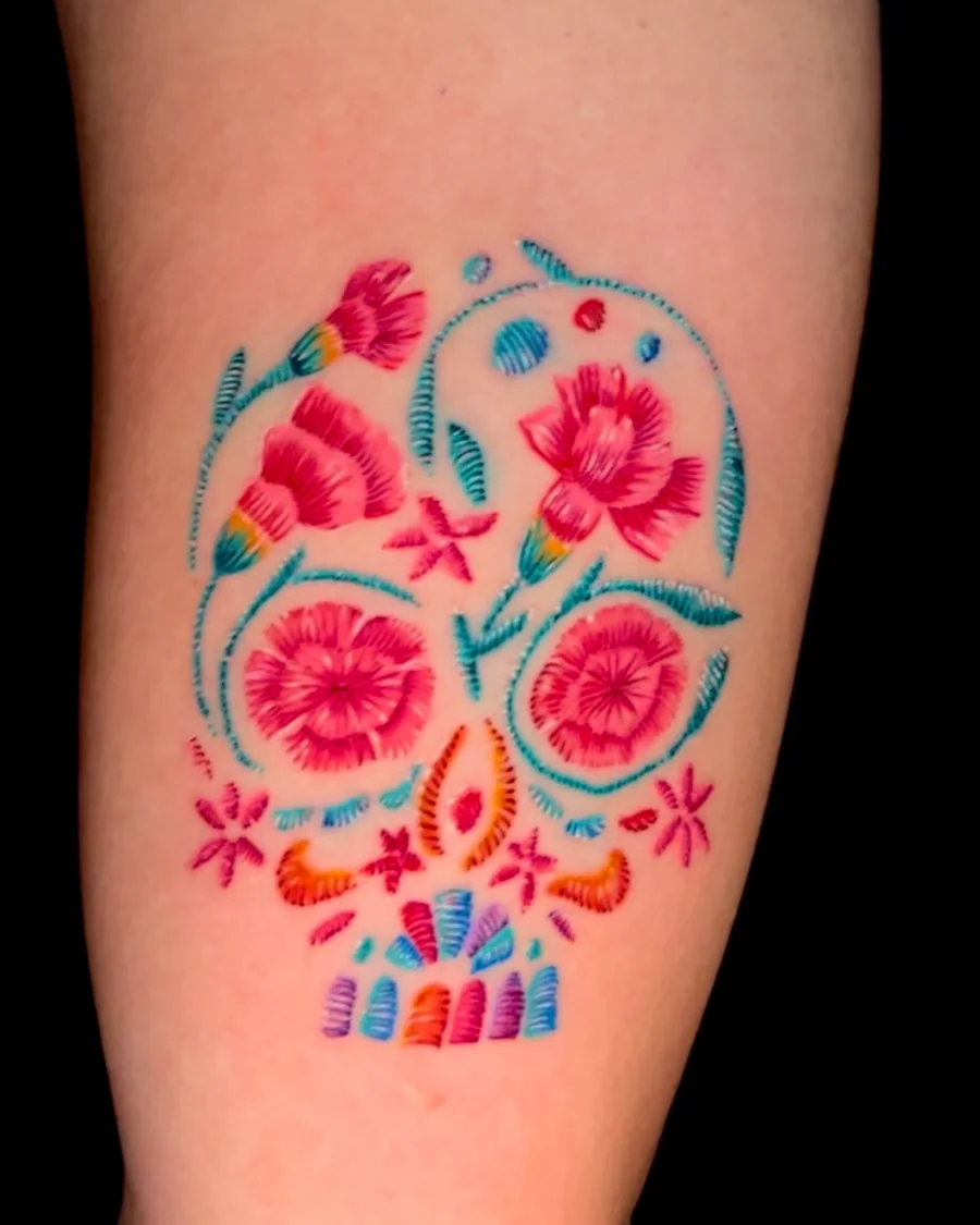 A colorful decorative skull formed from pink and red flowers, blue dots and turquoise ornamental lines.