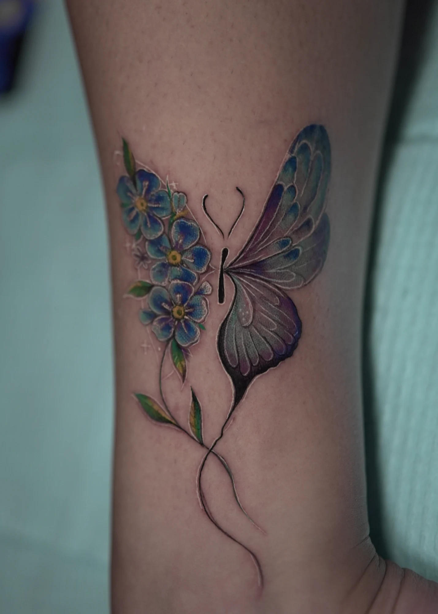 A purple butterfly wing paired with small blue flowers and a fine curved stem.