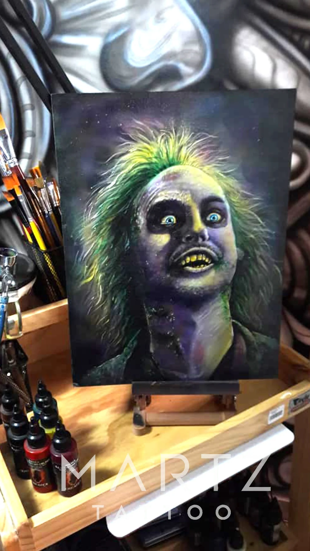 A painted Beetlejuice portrait with bright green hair, dark eyes and a striped jacket, displayed on an easel.