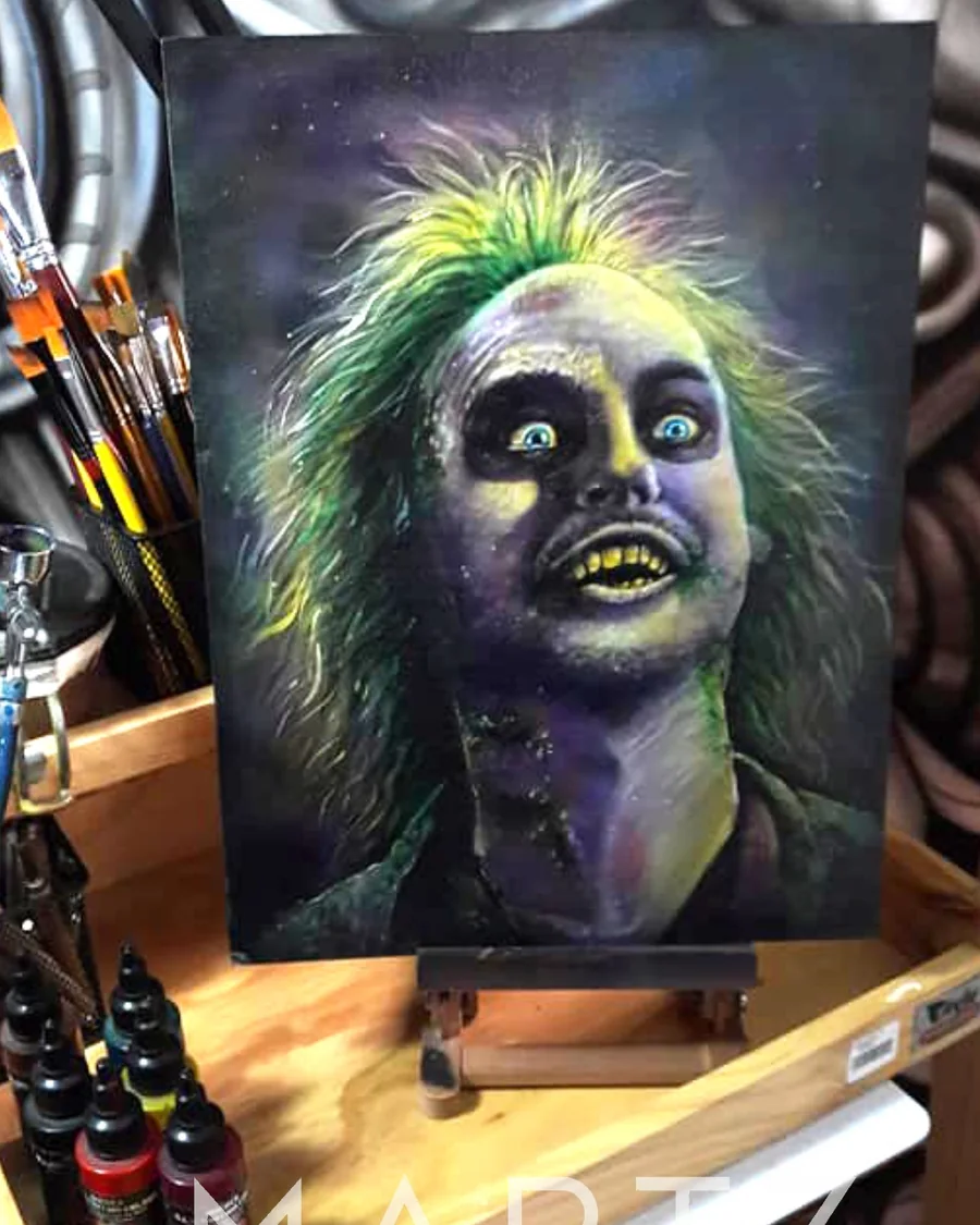 A painted Beetlejuice portrait with bright green hair, dark eyes and a striped jacket, displayed on an easel.