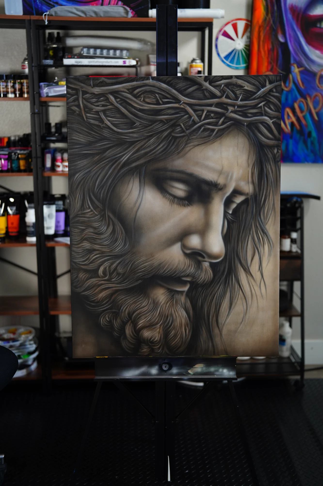 A monochrome painted portrait of Jesus wearing a crown of thorns, with his face lowered and eyes partly closed.
