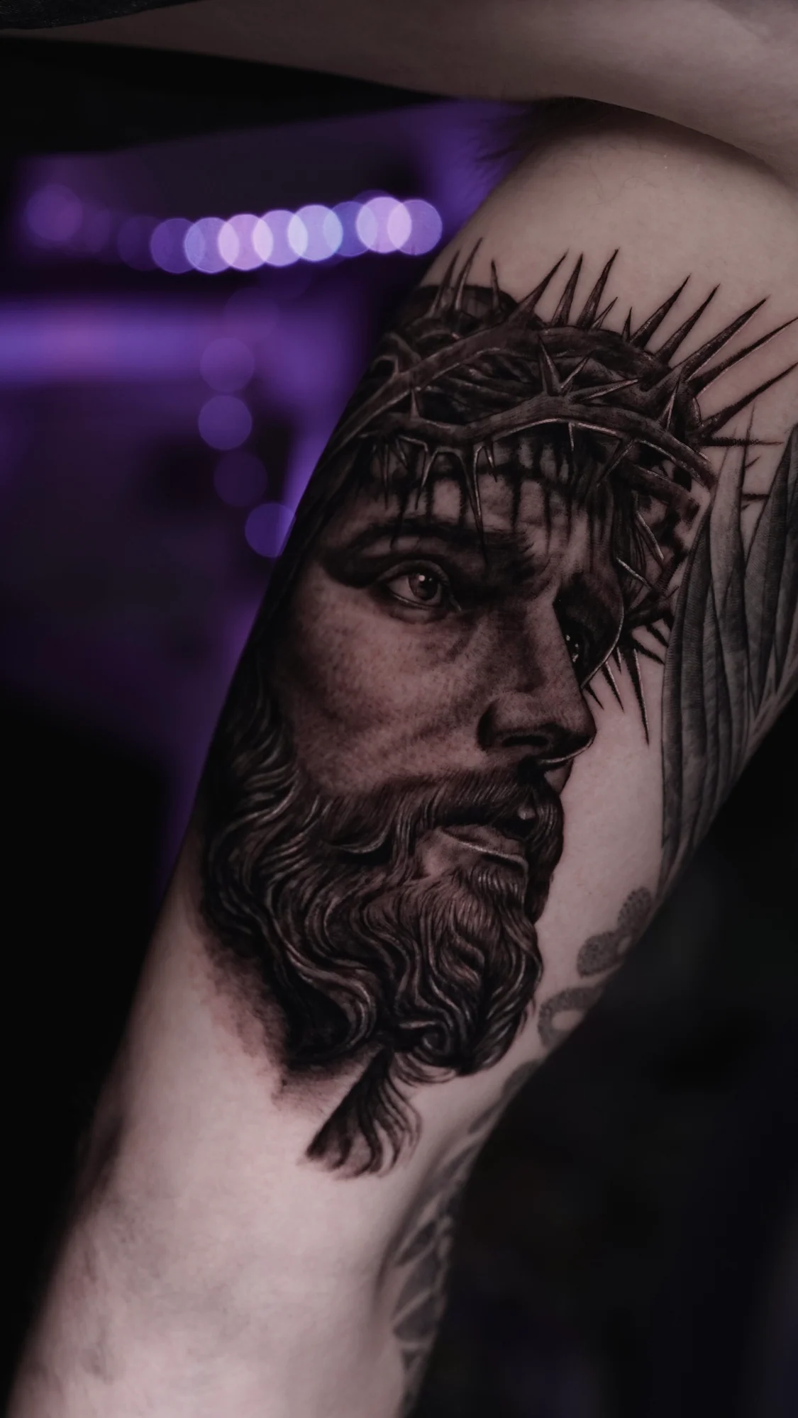 A black-and-gray realistic portrait tattoo of Jesus wearing a crown of thorns.