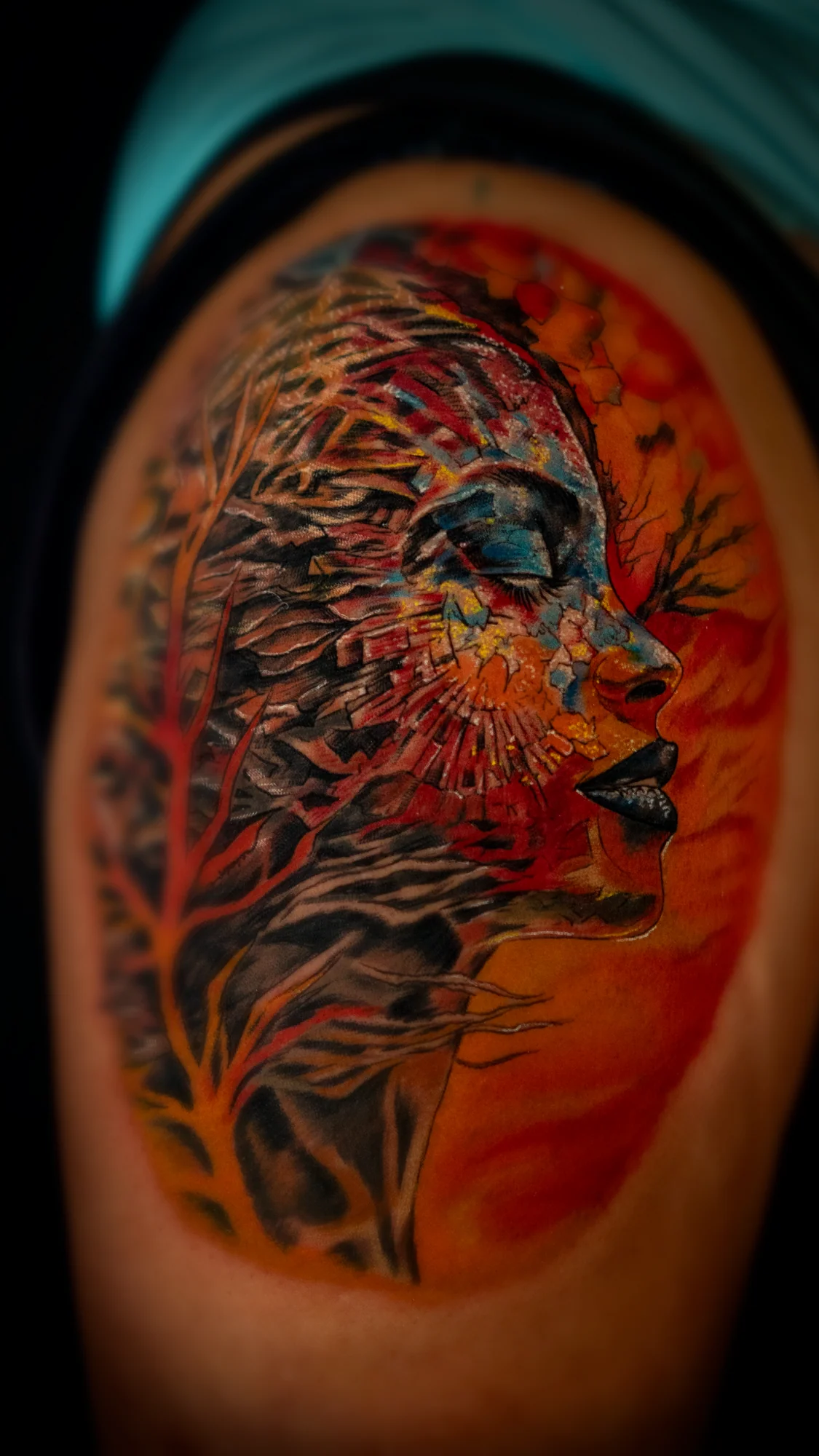 A vivid color portrait tattoo of a woman's profile layered with red, orange, blue and black painterly textures.