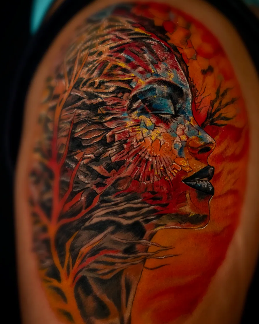 A vivid color portrait tattoo of a woman's profile layered with red, orange, blue and black painterly textures.