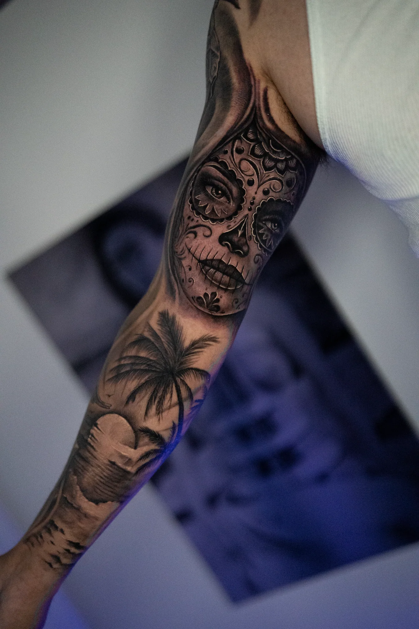 A black-and-gray sleeve combining a decorative sugar-skull portrait with palm trees and a tropical sunset.