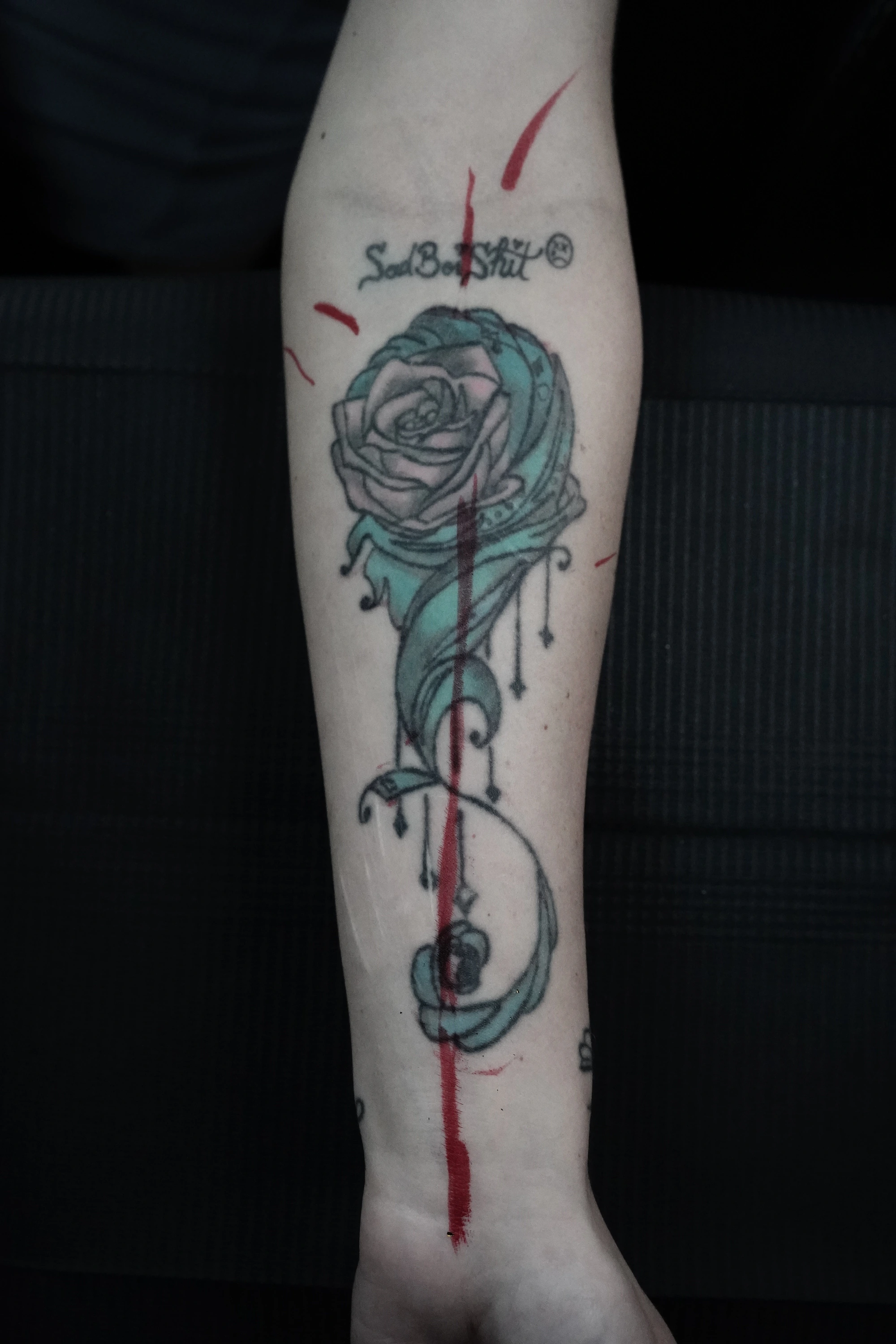Before: a rose with blue-green areas, lettering and lines extending along the forearm.