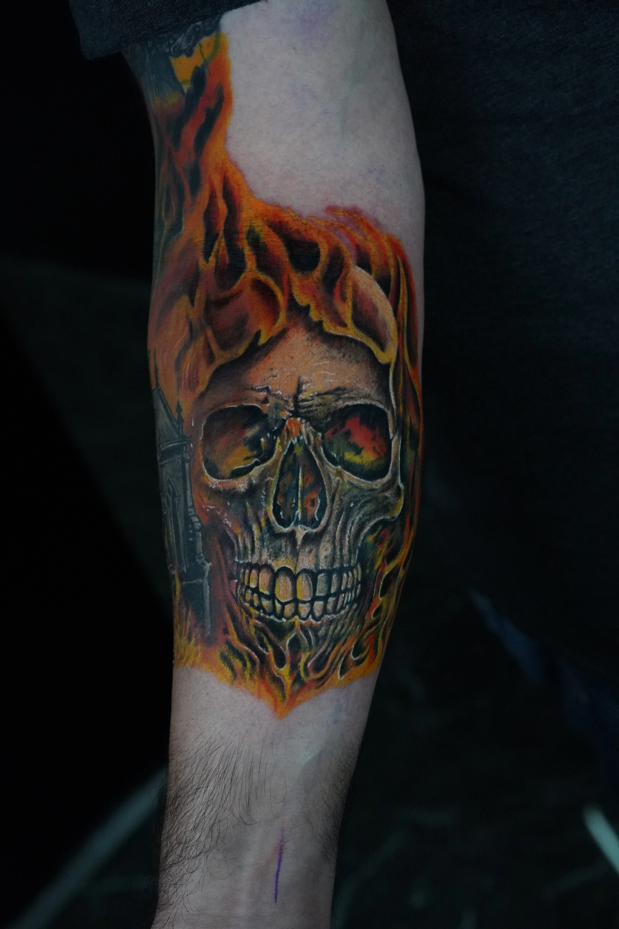 A finished forearm cover-up of a textured skull surrounded by orange, yellow, and red flames.