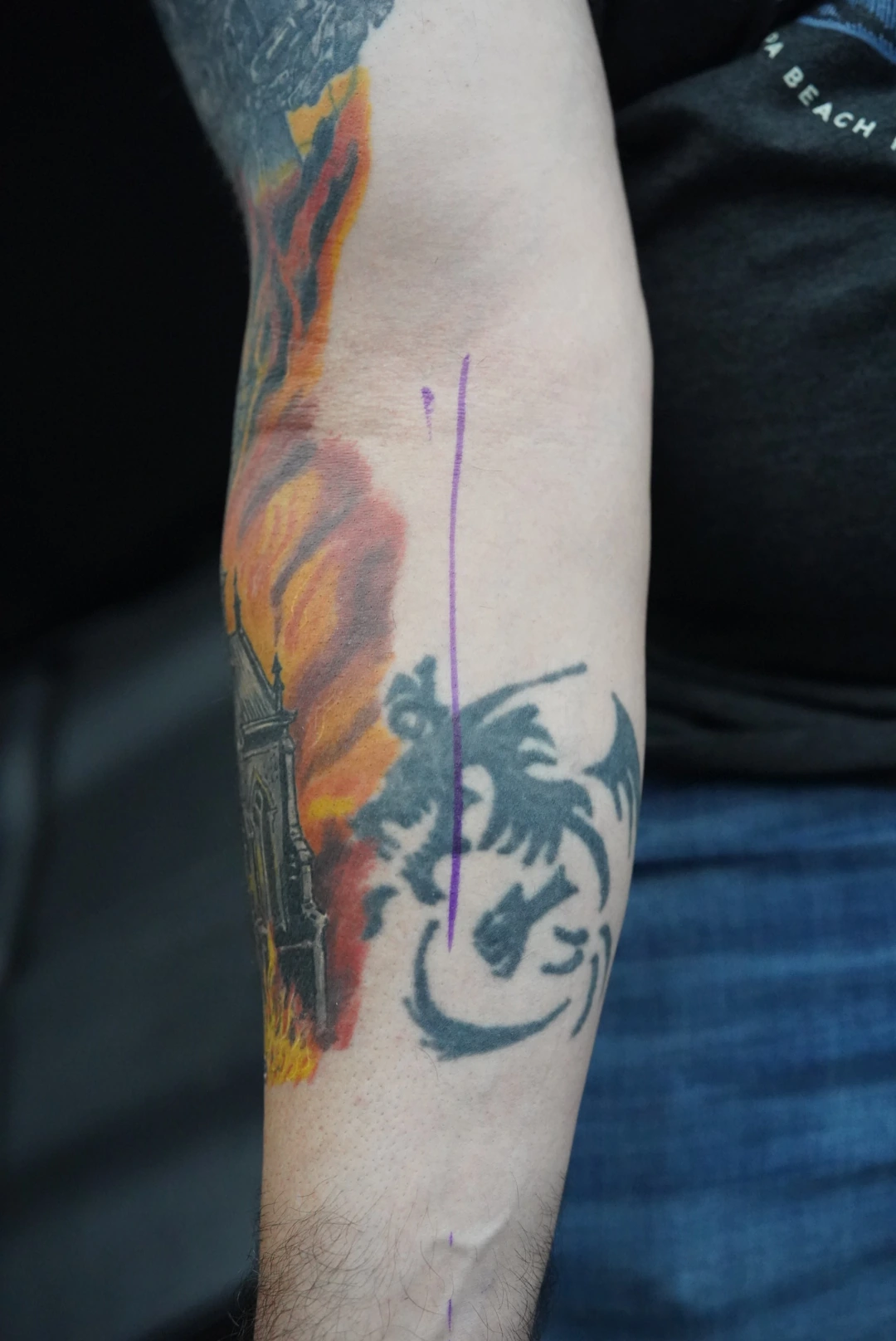 The earlier dark motif beside colored flames on the forearm.