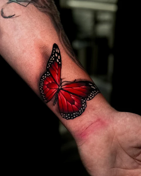 A red butterfly tattoo near the wrist, with dark wing edges and small pale markings.