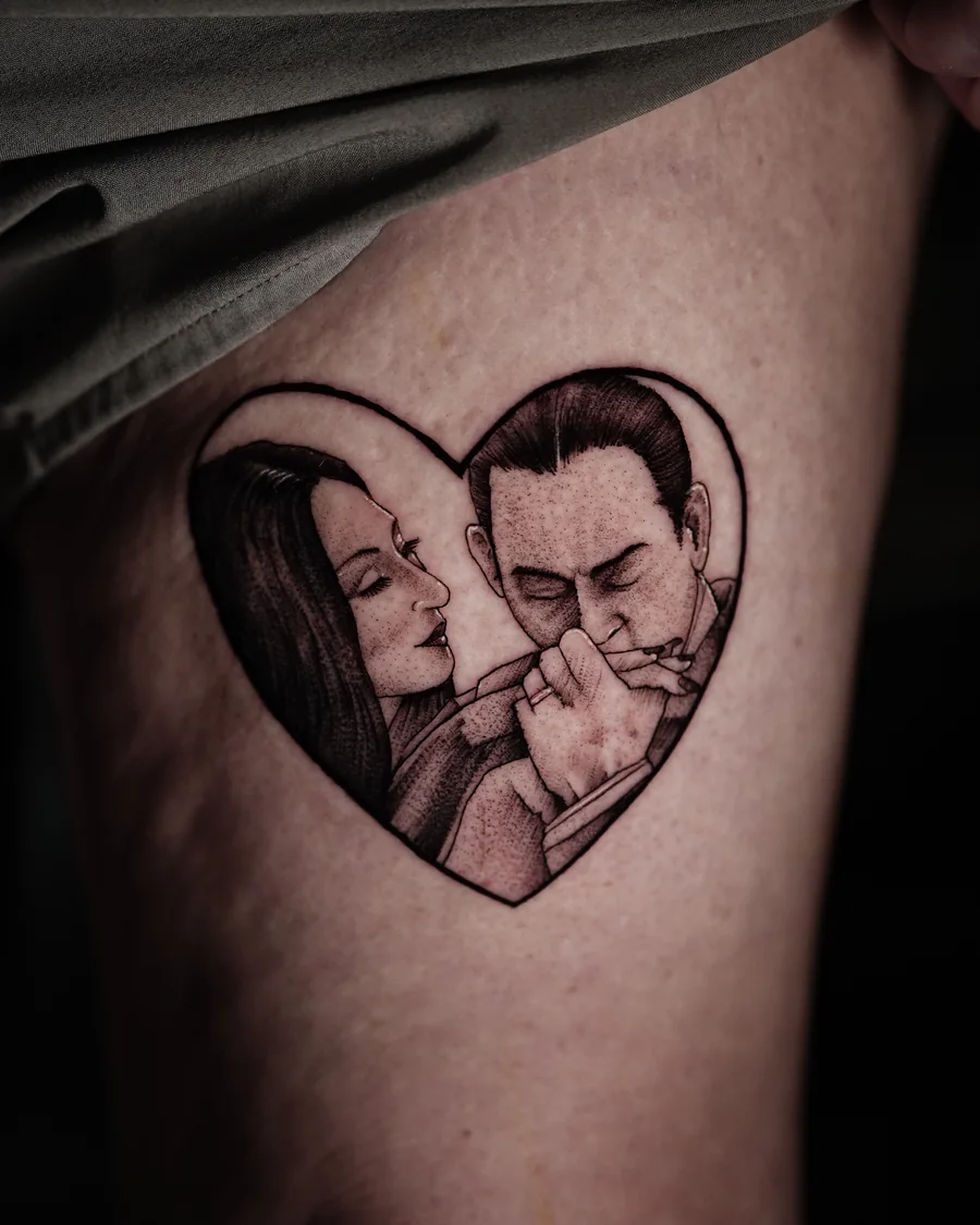 Gomez and Morticia Addams appear together inside a heart-shaped black-and-gray tattoo.