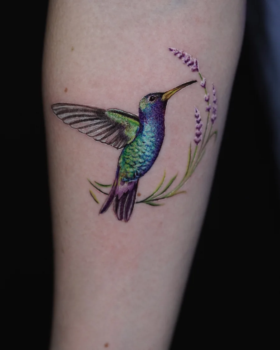 A colorful hummingbird tattoo reaching toward a slender flowering stem.