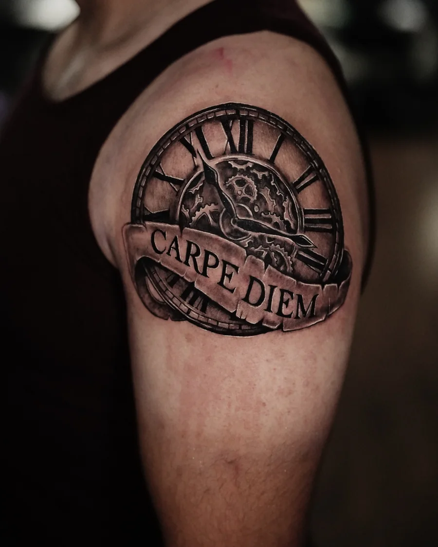 A circular clock tattoo with Roman numerals and a ribbon reading Carpe Diem on the upper arm.