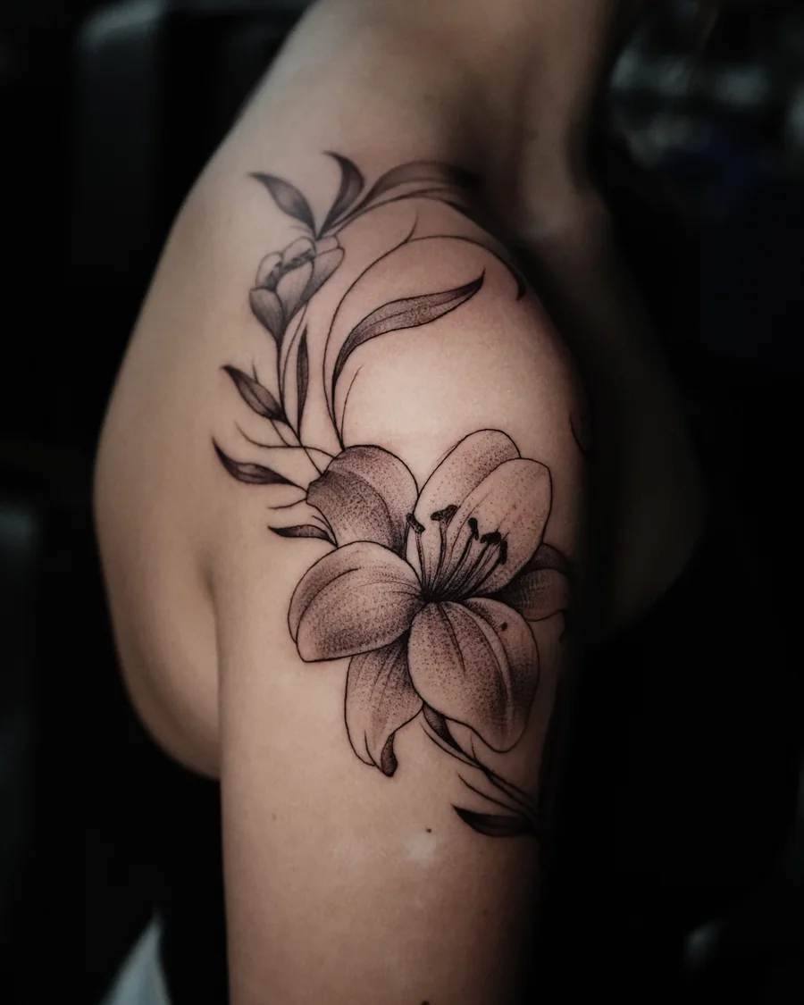 Large fine-line lilies and flowing leaves extending over the shoulder and toward the collarbone.