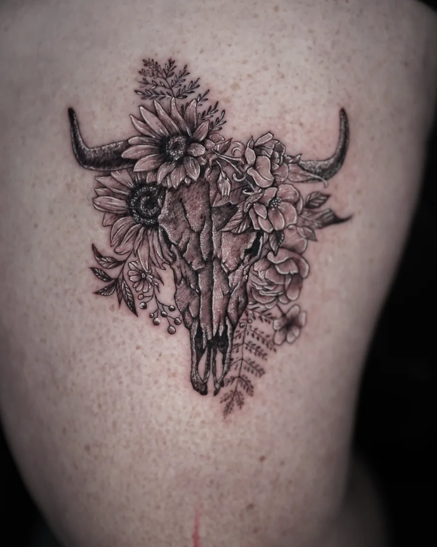 A horned cattle skull surrounded by detailed flowers, leaves and small buds in black linework.