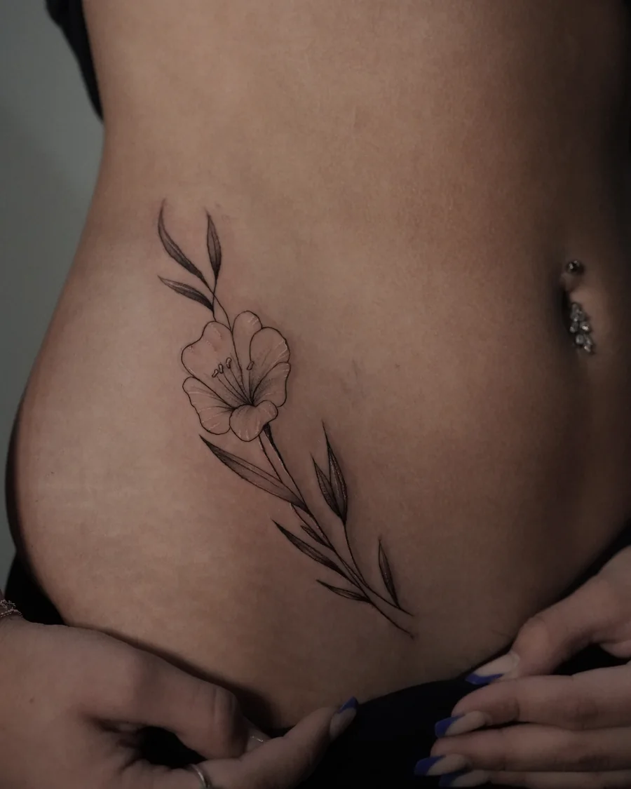 A single fine-line flower with long curved leaves placed along the side of the lower abdomen.