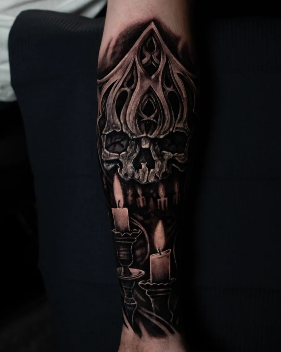 A black-and-gray calf tattoo of a skull beneath pointed Gothic ornament with glowing candles below.
