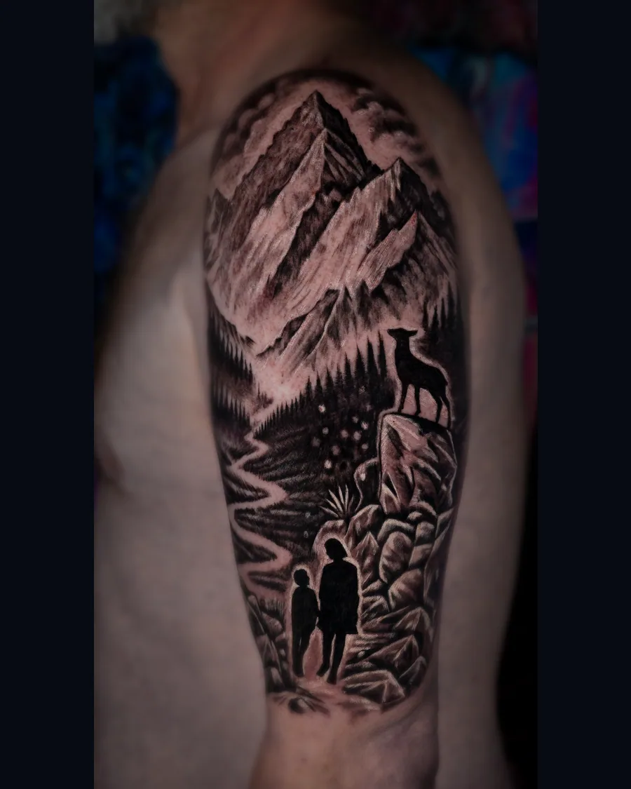 A black-and-gray mountain landscape tattoo with pine forest, a deer on a rock and adult-and-child silhouettes walking together.